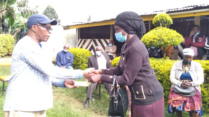 Prof. Reuben Marwanga hands over a school fees cheque to one of the beneficiary's parent at Nyansiongo town Wednesday. PHOTO/Dan Nyamanga.