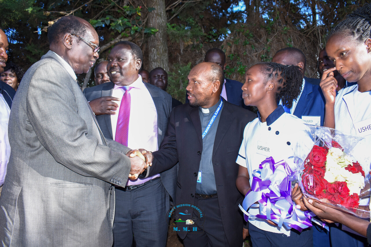 The Minister for Presidential Affairs of the Republic of South Sudan, Barnabas Benjamin (left), who led a delegation of leaders to Mercy Mission Hospital Eldama Ravine, being received by Fr. Francis Mugo, Mercy Mission Hospital Administrator; in the middle is Musa Sirma, Area Member of Parliament, and the nurse flower girls.  PHOTO/MMH.